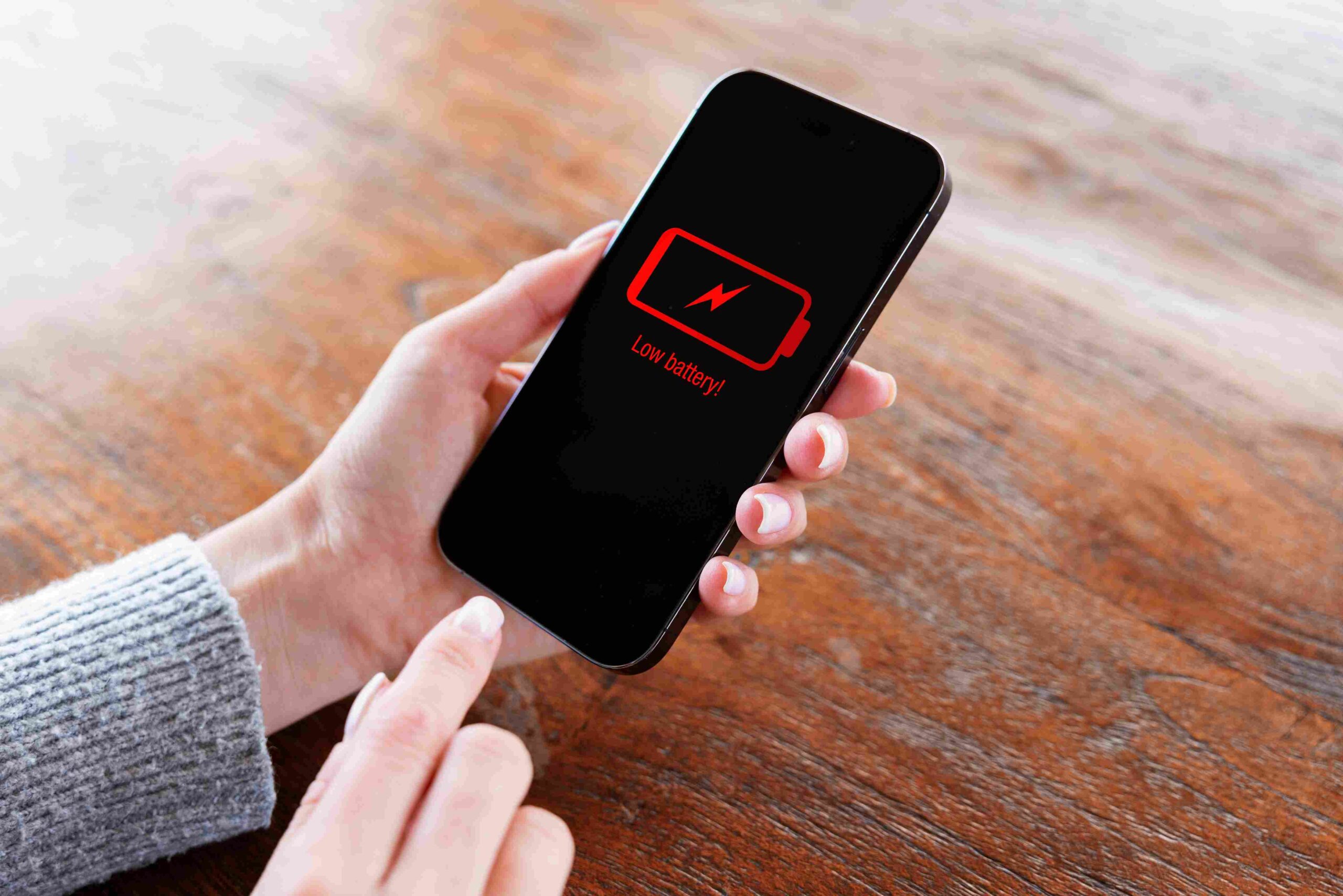 Osoba drži telefon sa upozorenjem o praznoj bateriji na ekranu