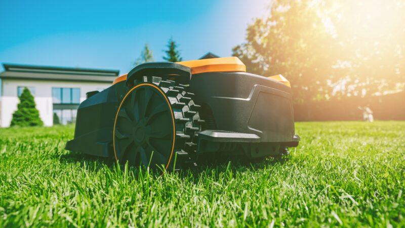 Robot kosilica radi na travnjaku ispred kuće po sunčanom danu