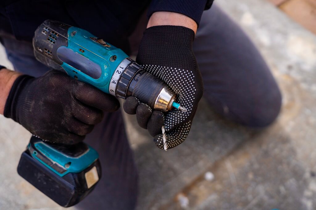 Radnik koristi akumulatorsku bušilicu sa zaštitnim rukavicama