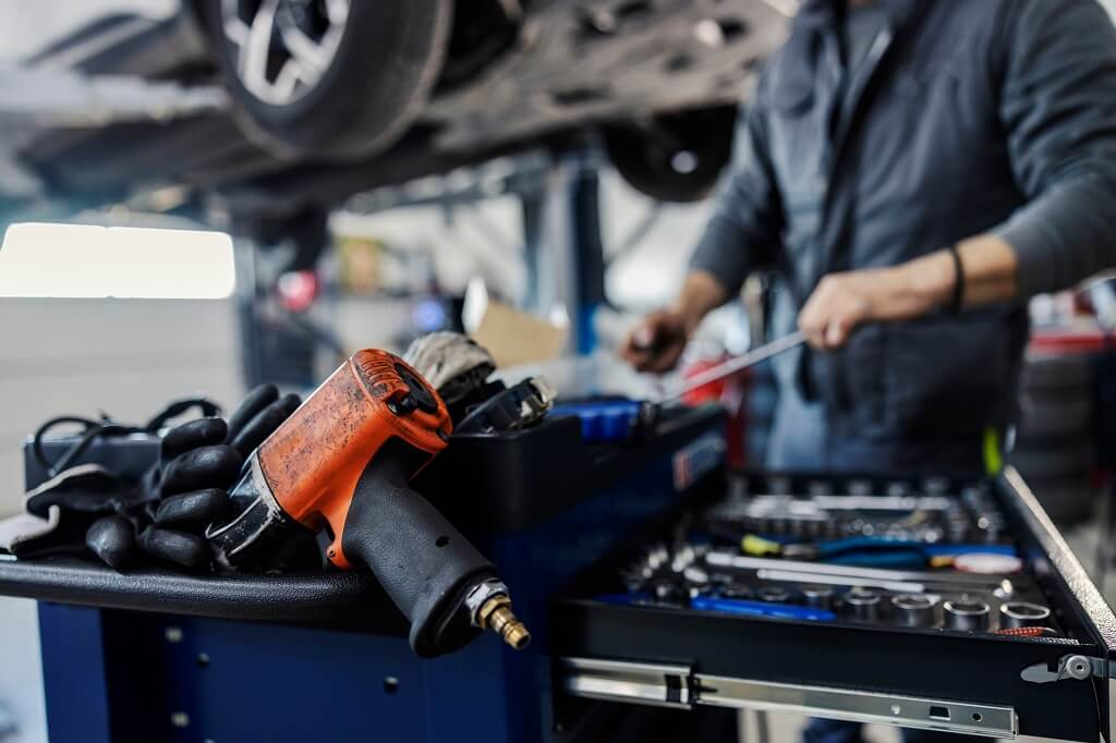 Automehaničar radi u servisu sa pneumatskim alatom i setom ključeva