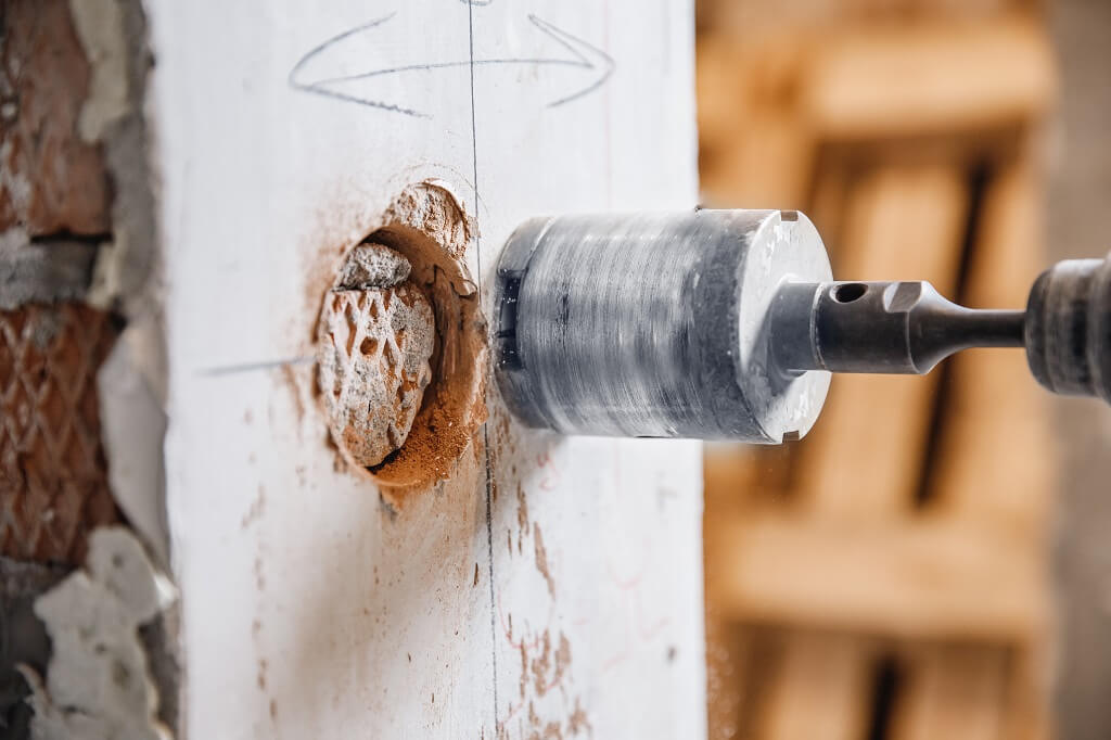 Kruna za beton u procesu bušenja zida sa jasno vidljivim otvorom i prašinom